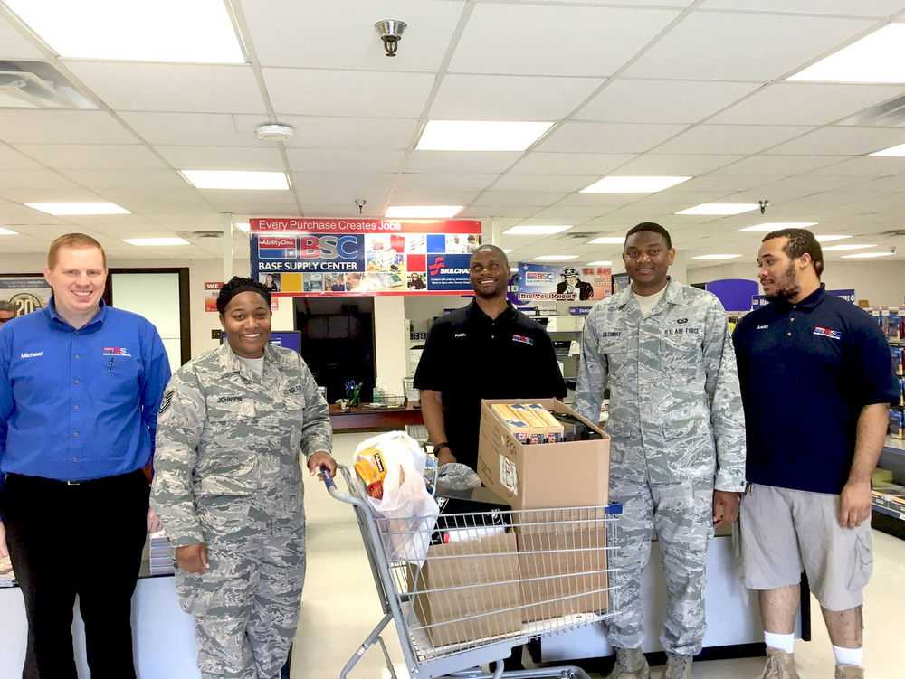 BISM BSC staff members and two military shoppers inside BSC pose in front of shopping cart loaded with office supplies.
