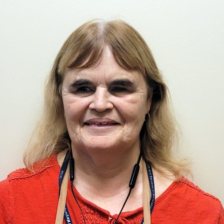 Close-up photo of Alice in a red shirt, beige work apron and beautiful smile.