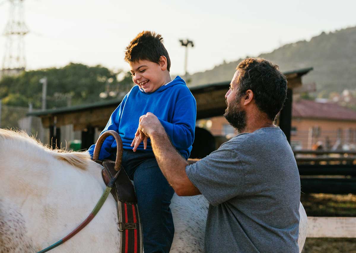 Sight-impaired child riding a horse with help from volunteer.