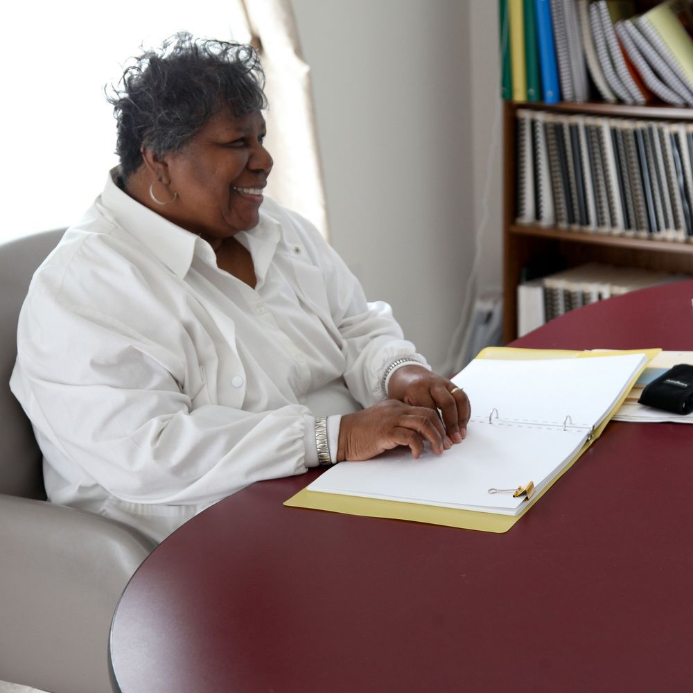 joyous woman wearing white blouse reading Braille at desk