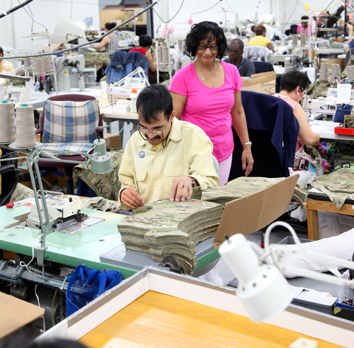 blind female is sewing jacket while supervisor looks on