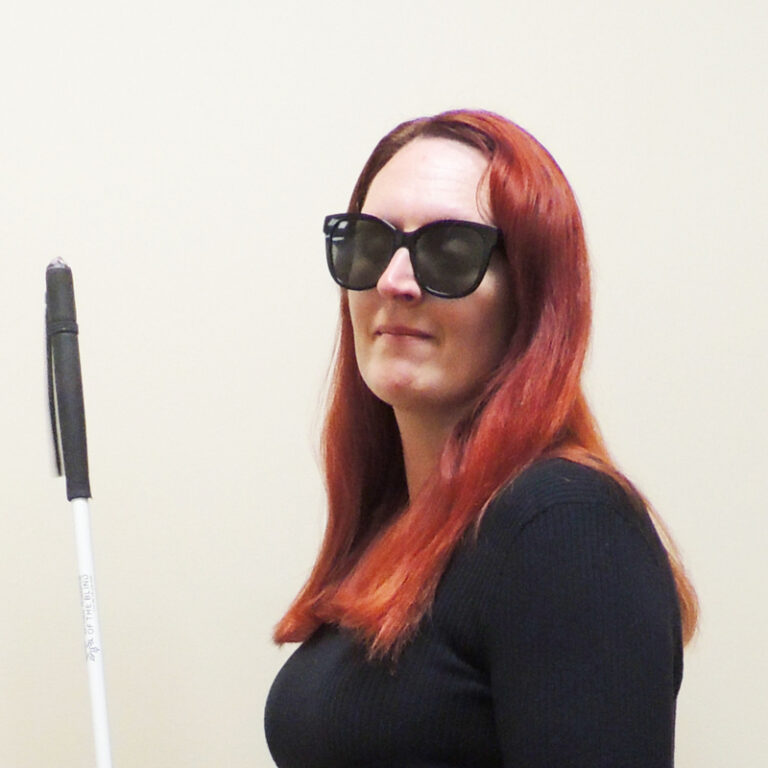 Laura smiles knowingly as she stands in the BISM office wearing a black sweater and dark glasses.