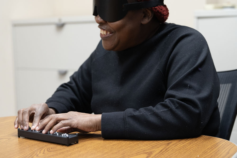 Woman sitting at desk smiling as she works with Braille box