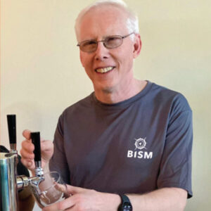 Dr. Michael Gosse, president of BISM, dressed in blue BISM t-shirt, is drawing a beer from the tap at Checkerspot Brewery.