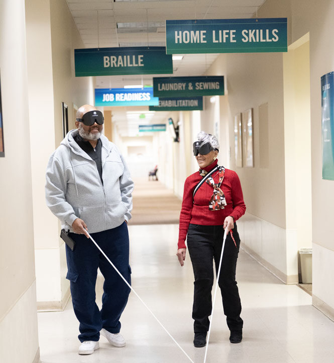 Two seniors walking through hallway with long white canes
