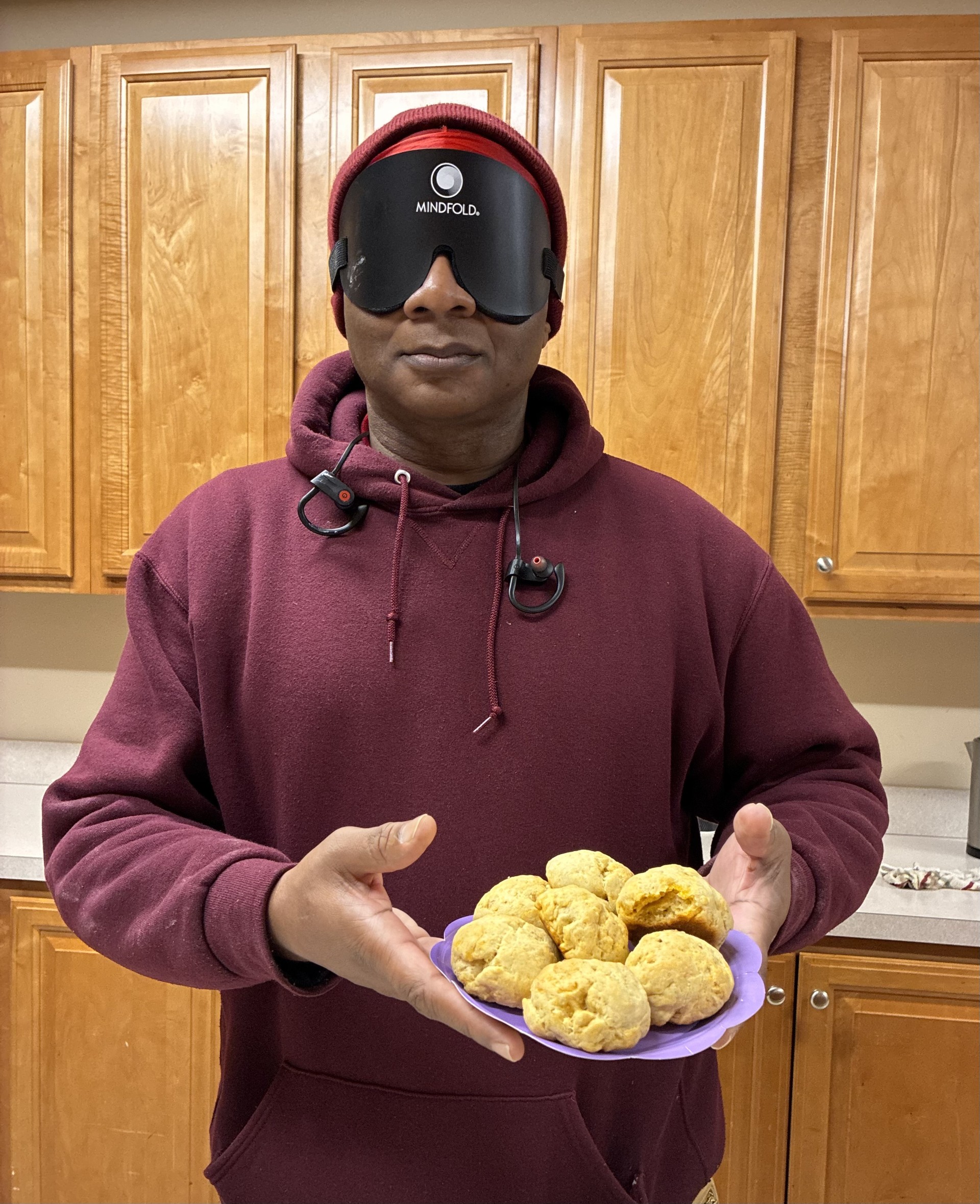 BISM SAIL student wearing sleep shades holds up his finished biscuits in front of him.