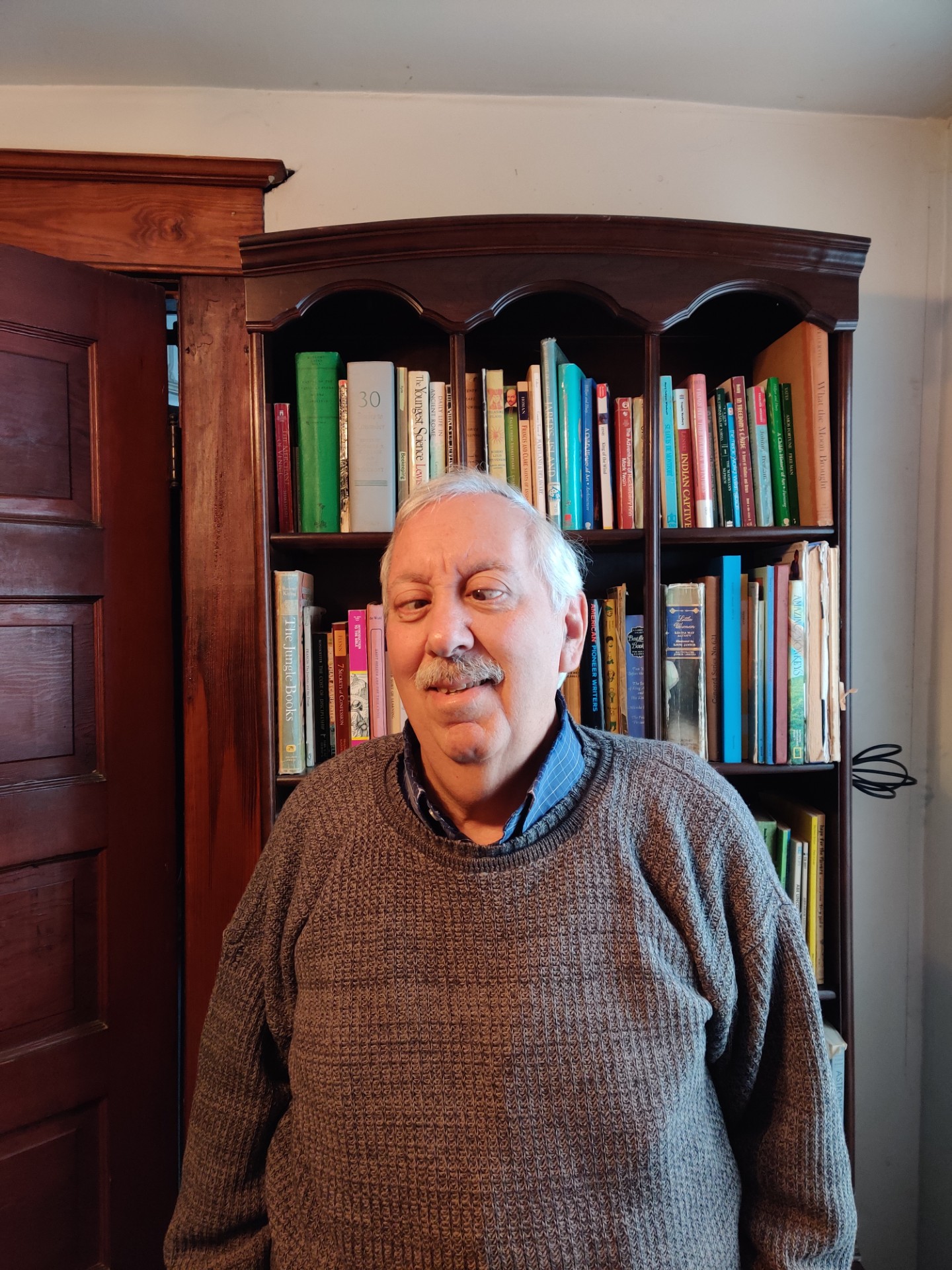 Alfred smiling and standing in front of a book shelf.